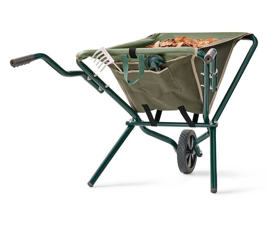 Eine grüne Schubkarre steht auf einem weißen Hintergrund. Die Schubkarre ist mit Blättern gefüllt und hat Gartengeräte in den Taschen.