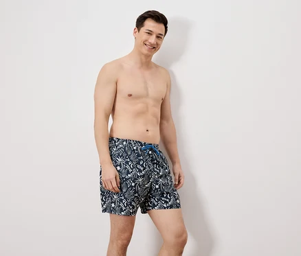 Ein Mann mit Badehose steht vor einer weißen Wand.