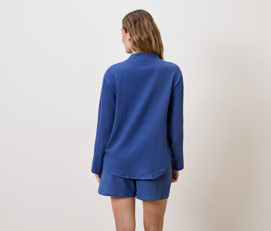 Rückansicht einer Frau mit langen, braunen Haaren, die ein blaues, langärmeliges Hemd und Shorts trägt.