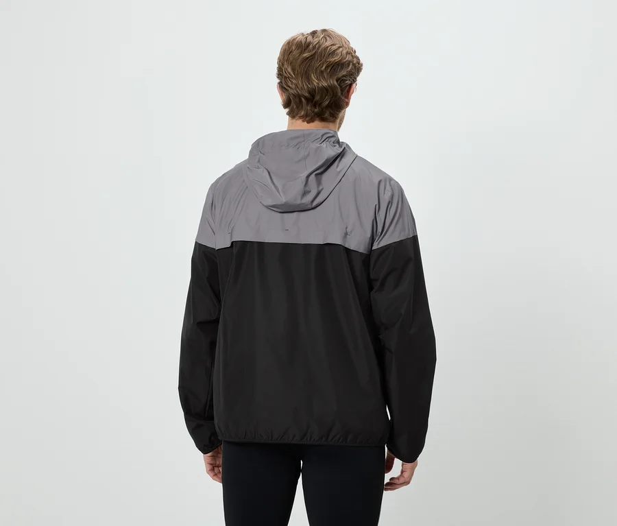 Rückansicht eines Mannes mit lockigem Haar, der eine grau-schwarze Regenjacke und schwarze Hose vor einem weißen Hintergrund trägt.