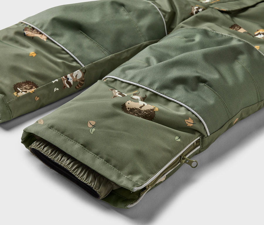 Nahaufnahme einer olivgrünen Hose mit Taschen und Reißverschluss, bedruckt mit Waschbären, Igeln und Blättern.
