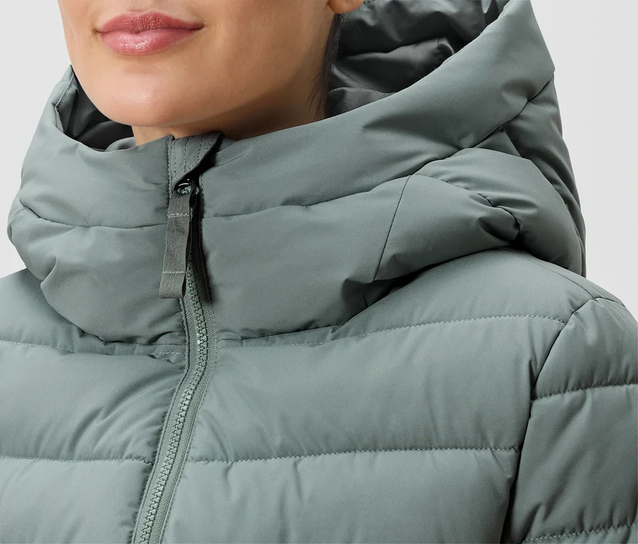 Nahaufnahme einer Frau, die eine grüne, gesteppte Daunenjacke mit Kapuze und Reißverschluss trägt.
