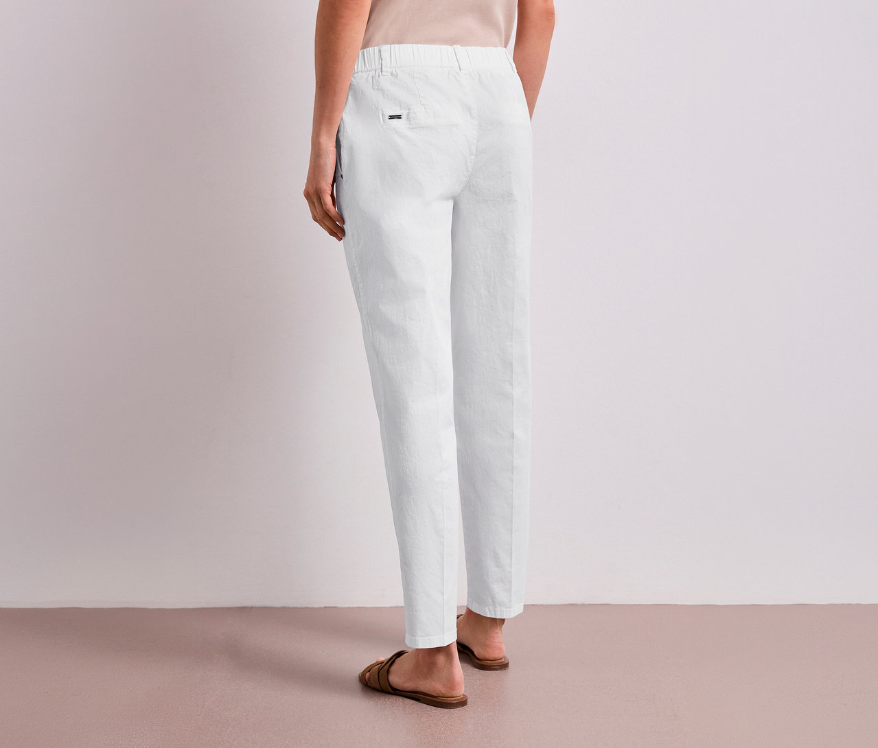 Eine Person steht mit dem Rücken zur Kamera und trägt eine weiße Street One Chino und braune Sandalen.
