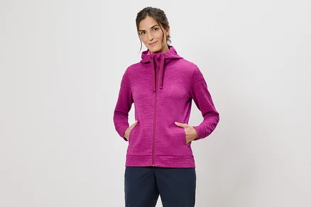 Frau mit Kapuzenpullover in Pink mit Händen in den Taschen vor einem weißen Hintergrund.