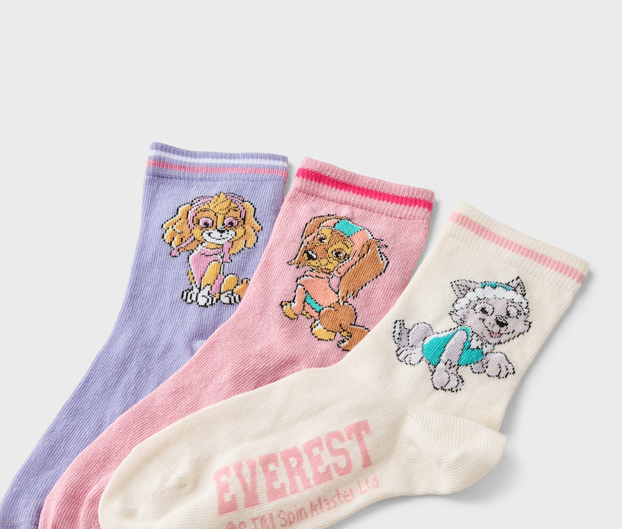Drei Socken liegen nebeneinander: eine lavendelfarbene Socke mit einem Skye-Motiv, eine rosa Socke mit einem Motiv von Everest und eine cremefarbene Socke mit einem Everest-Motiv.