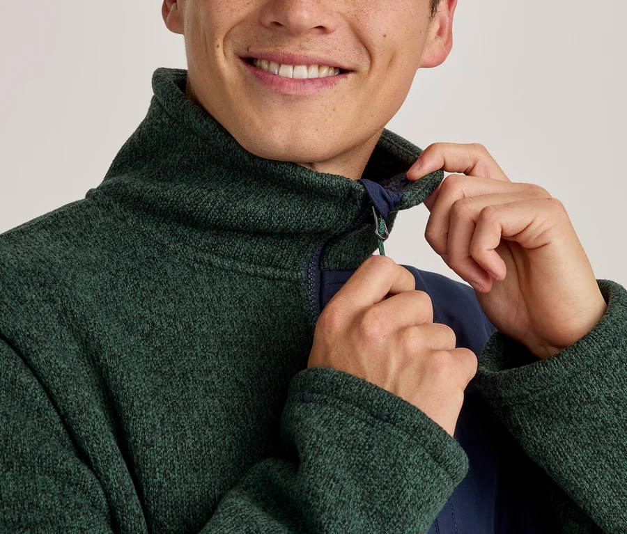 Lächelnder Mann, der den Kragen einer grünen, strukturierten Fleecejacke mit marineblauem Innenfutter zurechtrückt.