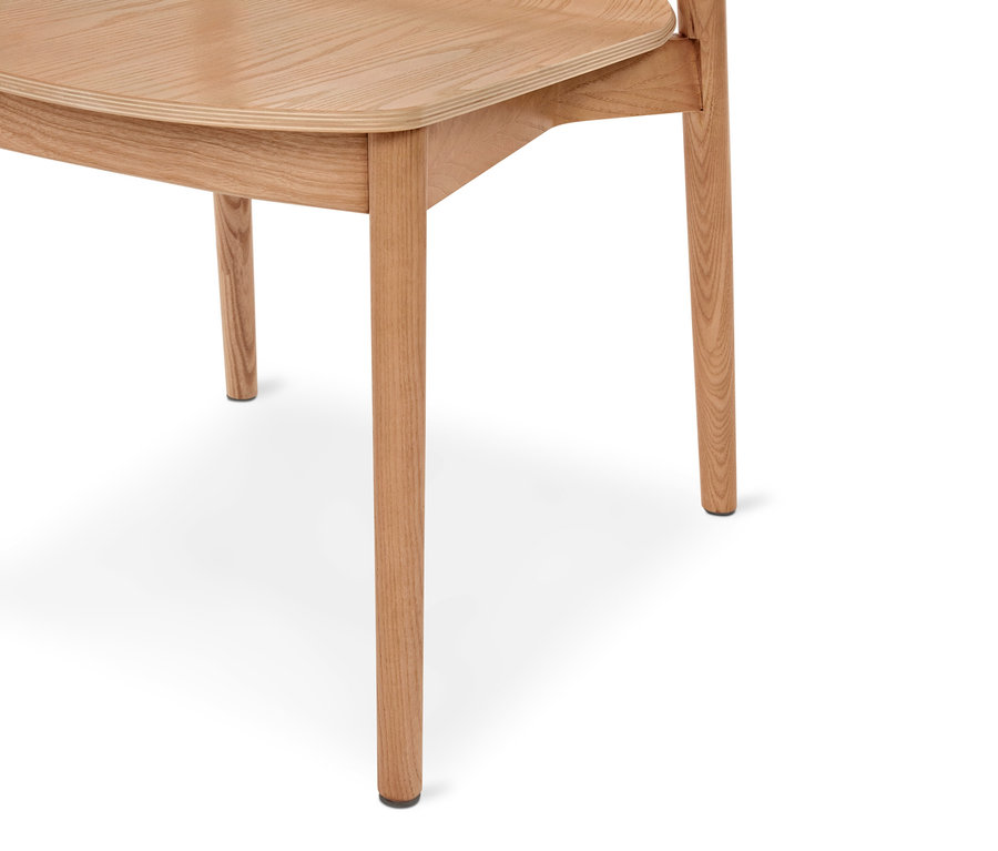 Unterer Teil eines hellen Holzstuhls mit geschwungener Sitzfläche und schlanken Beinen, mit schwarzen Fußkappen, vor weißem Hintergrund.