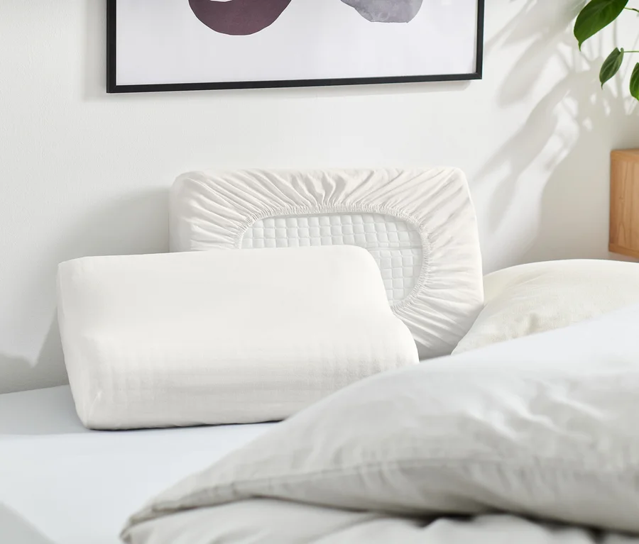 Mehrere weiße Kissen und ein weißer Kissenbezug liegen auf einem Bett.