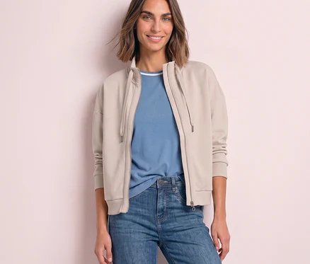 Lächelnde Frau in einer beigen, offenen Street One Sweatjacke über einem blauen T-Shirt und Jeans.