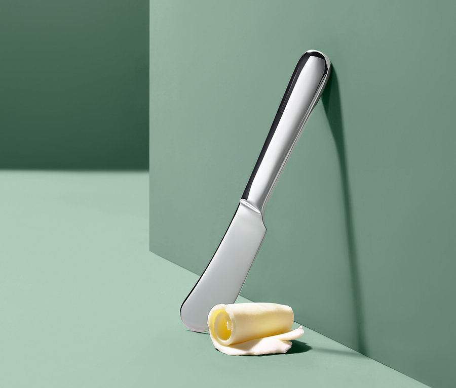 Ein silbernes Buttermesser und eine Butterrolle lehnen an einer grünen Wand.