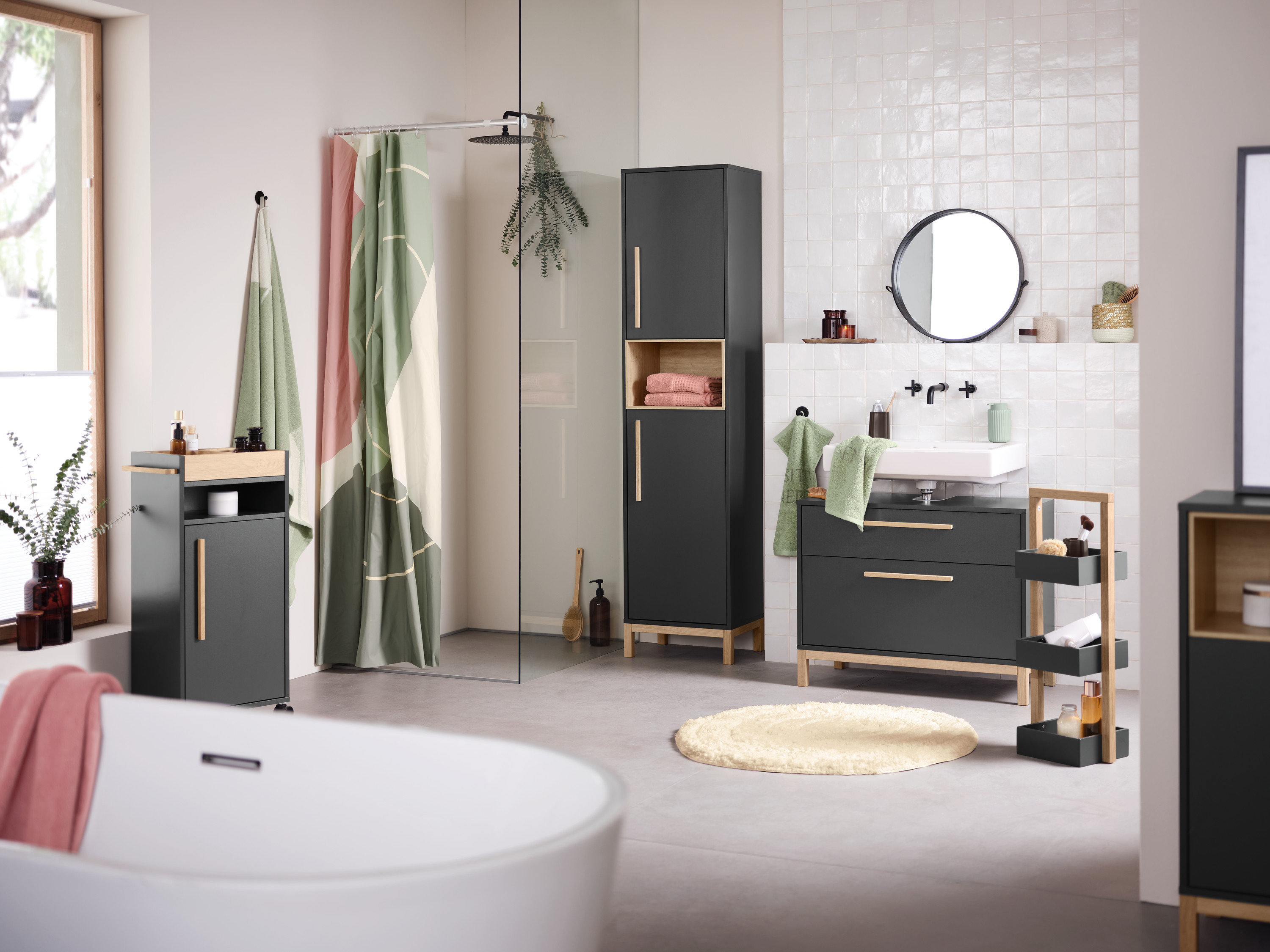 Badezimmer Interieur mit Waschbecken, Spiegel und Eklund Badschränken in Anthrazit. Im Vordergrund befindet sich eine Badewanne.