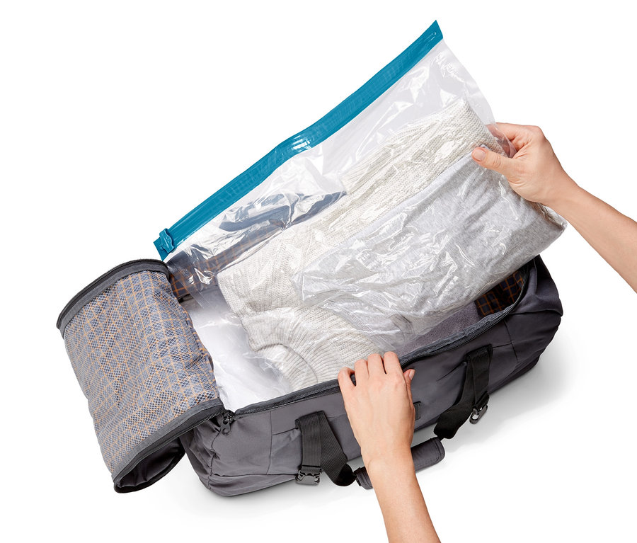 Hände legen Kleidung in einen offenen grauen Reisekoffer mit einem von 3 Vakuum-Reisebeuteln.