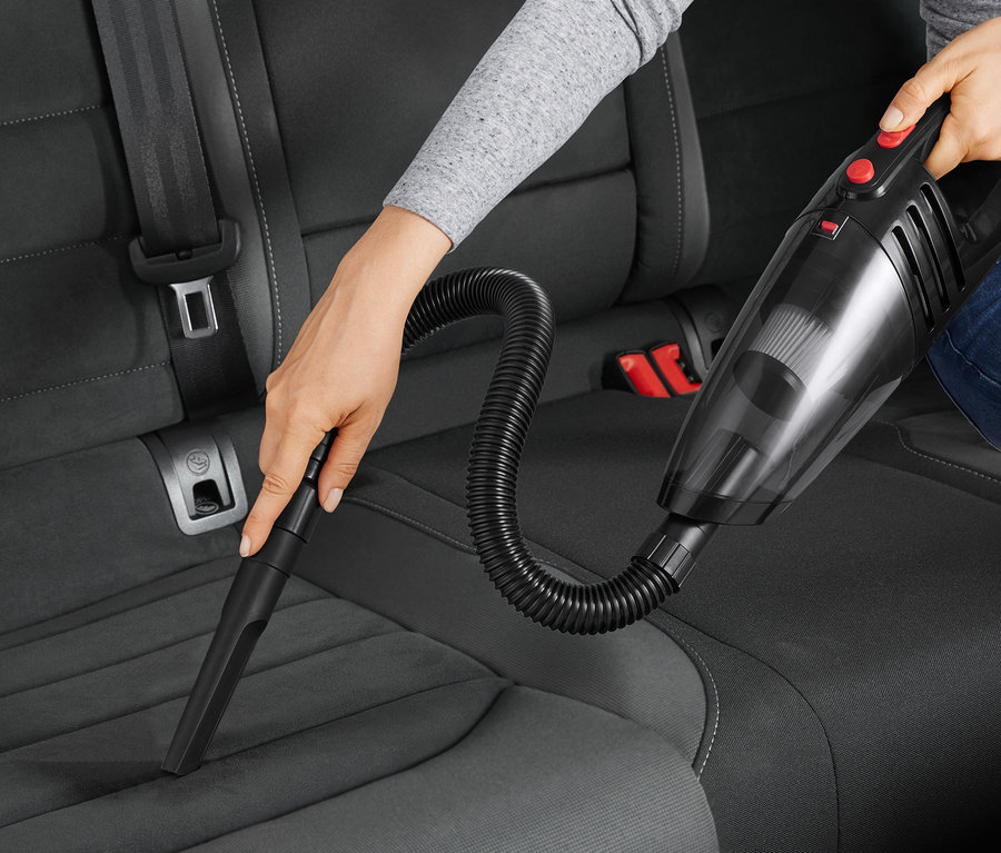 Frau saugt den Autositz mit einem Autostaubsauger.