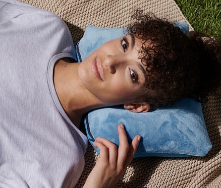Frau liegt auf Decke und benutzt blaues 2-in-1-Nackenkissen.