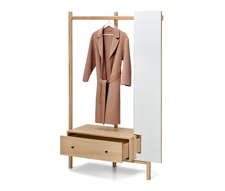 Ein hellbrauner Mantel hängt an einem weißen Bügel an einer hölzernen Garderobe mit offener Schublade und Spiegel.