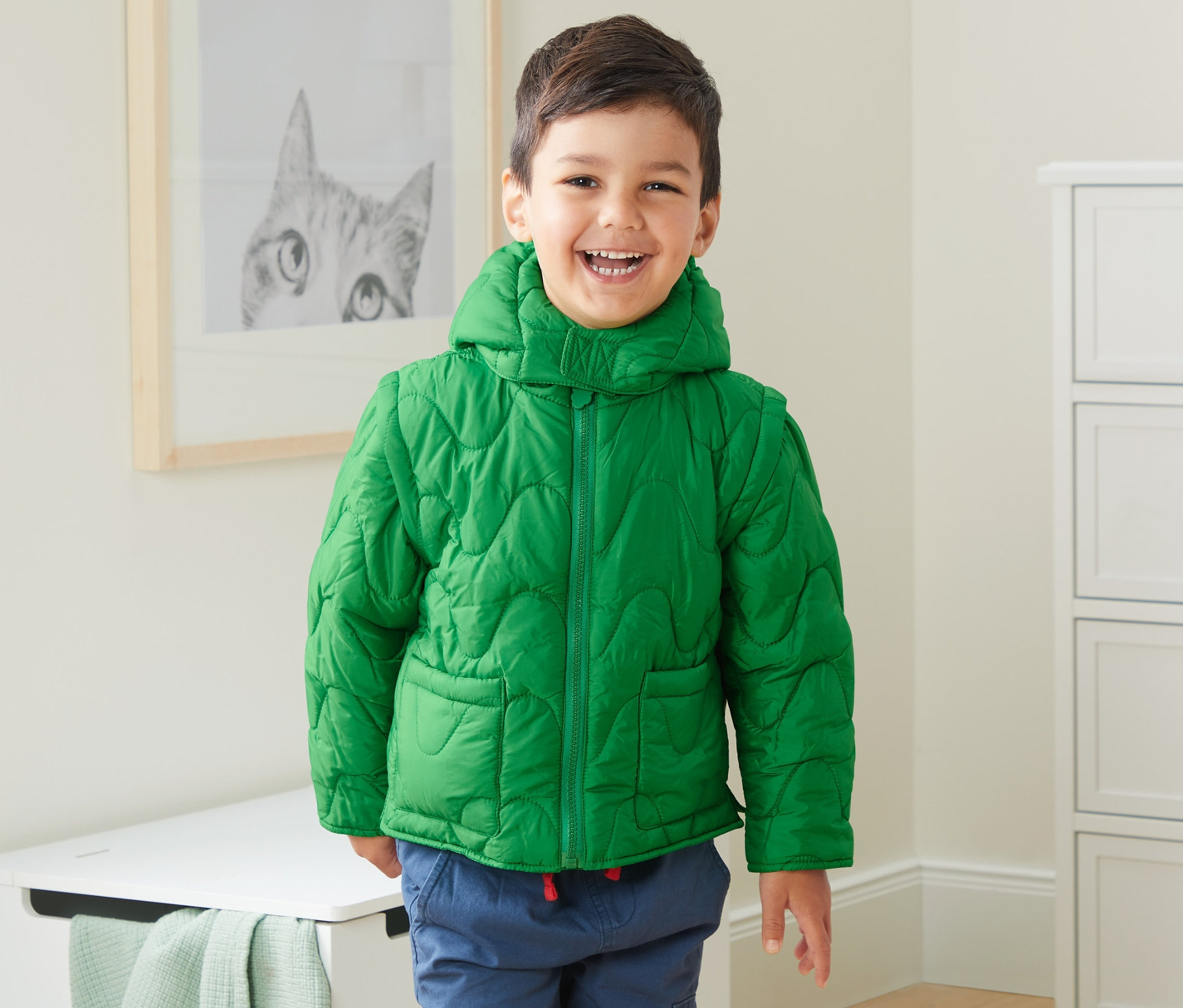 Lachender Junge trägt grüne Steppjacke aus recyceltem Material.