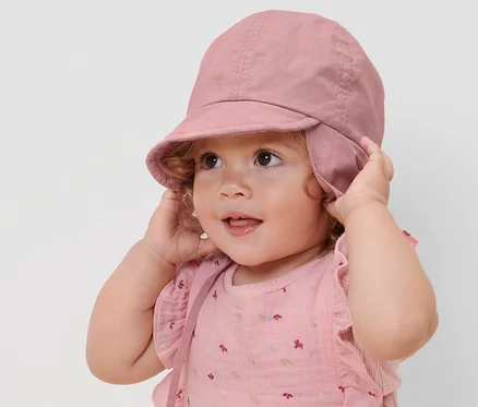 Ein Kind justiert eine rosa Kinder-Sonnenmütze mit UV-Schutzfaktor 80.