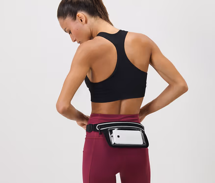 Frau justiert Laufgürtel für Smartphones um ihre Taille. Sie trägt einen Sport-BH und Leggings.