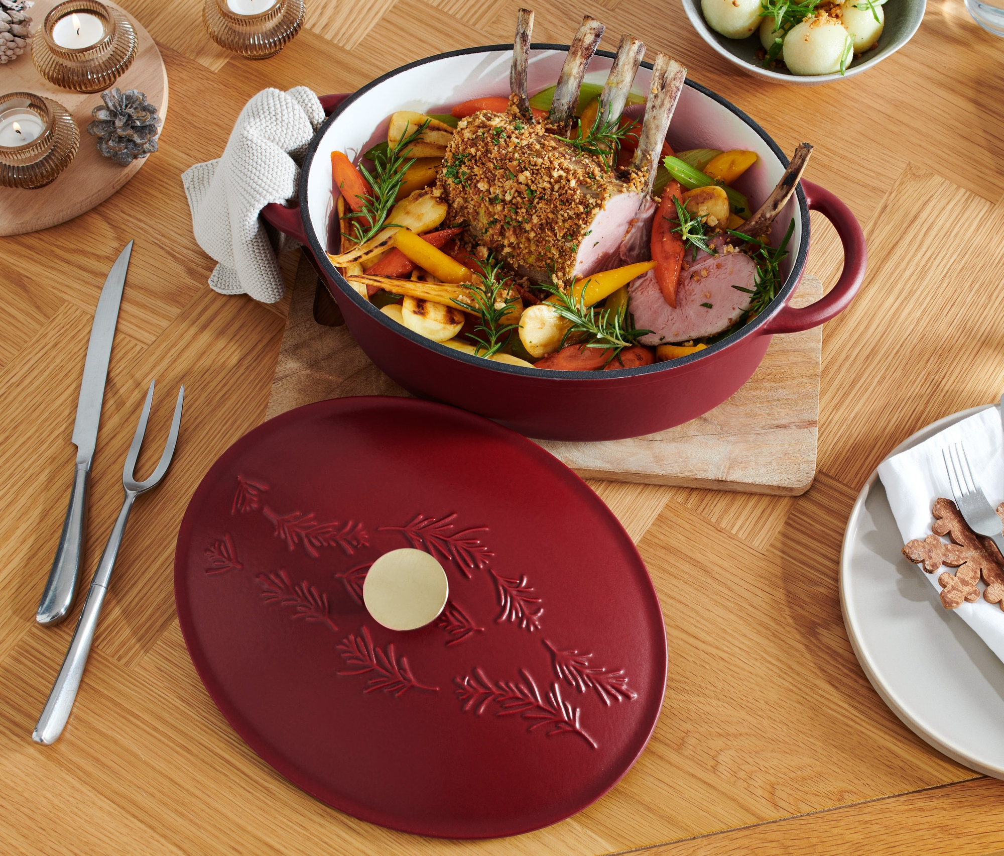 Braten mit Wurzelgemüse in einem roten, ovalen Gusseisen-Bräter auf einem Holztisch.