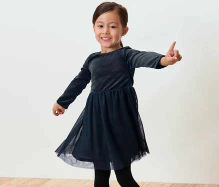 Ein lächelndes Mädchen im Kinder-Tüllkleid posiert vor hellem Hintergrund.