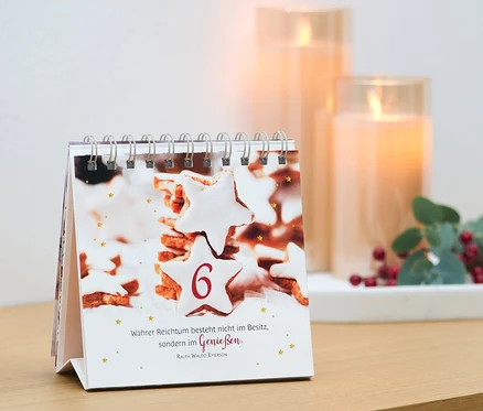 Ein Tischkalender mit einem Bild von Keksen und der Zahl 6, daneben Kerzen und Dekoration. Buch/Aufsteller: »Adventszauber«