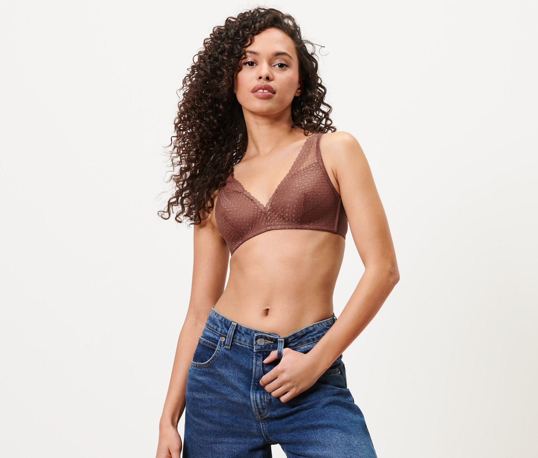 Frau posiert in kastanienbraunem Softschalen-BH und blauen Jeans.