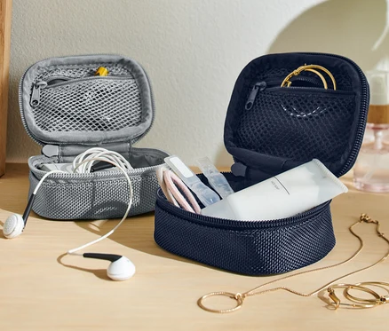 Zwei offene Mini-Reise-Ordnungstaschen, eine graue mit weißen Kopfhörern und eine marineblaue mit Kosmetika und Goldschmuck.