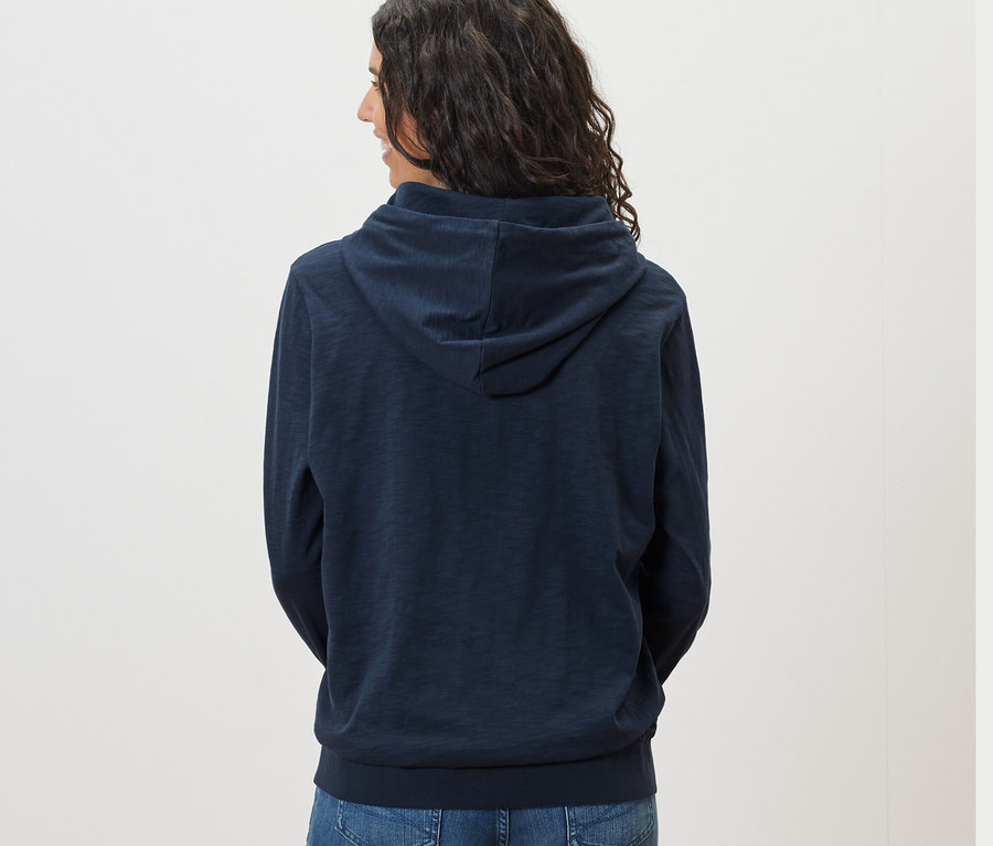 Rückansicht einer Frau mit dunklen Haaren in einem marineblauen Jersey-Hoodie.