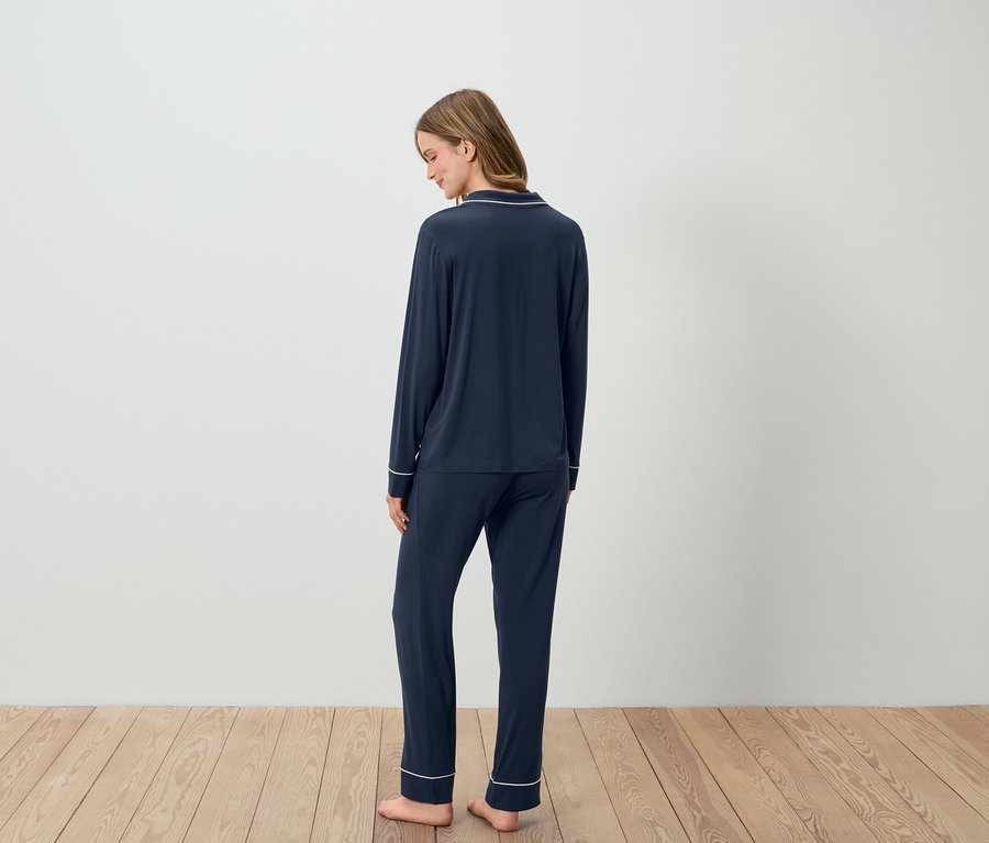 Frau steht mit dem Rücken zum Betrachter und trägt einen dunkelblauen Pyjama mit weißen Paspeln.