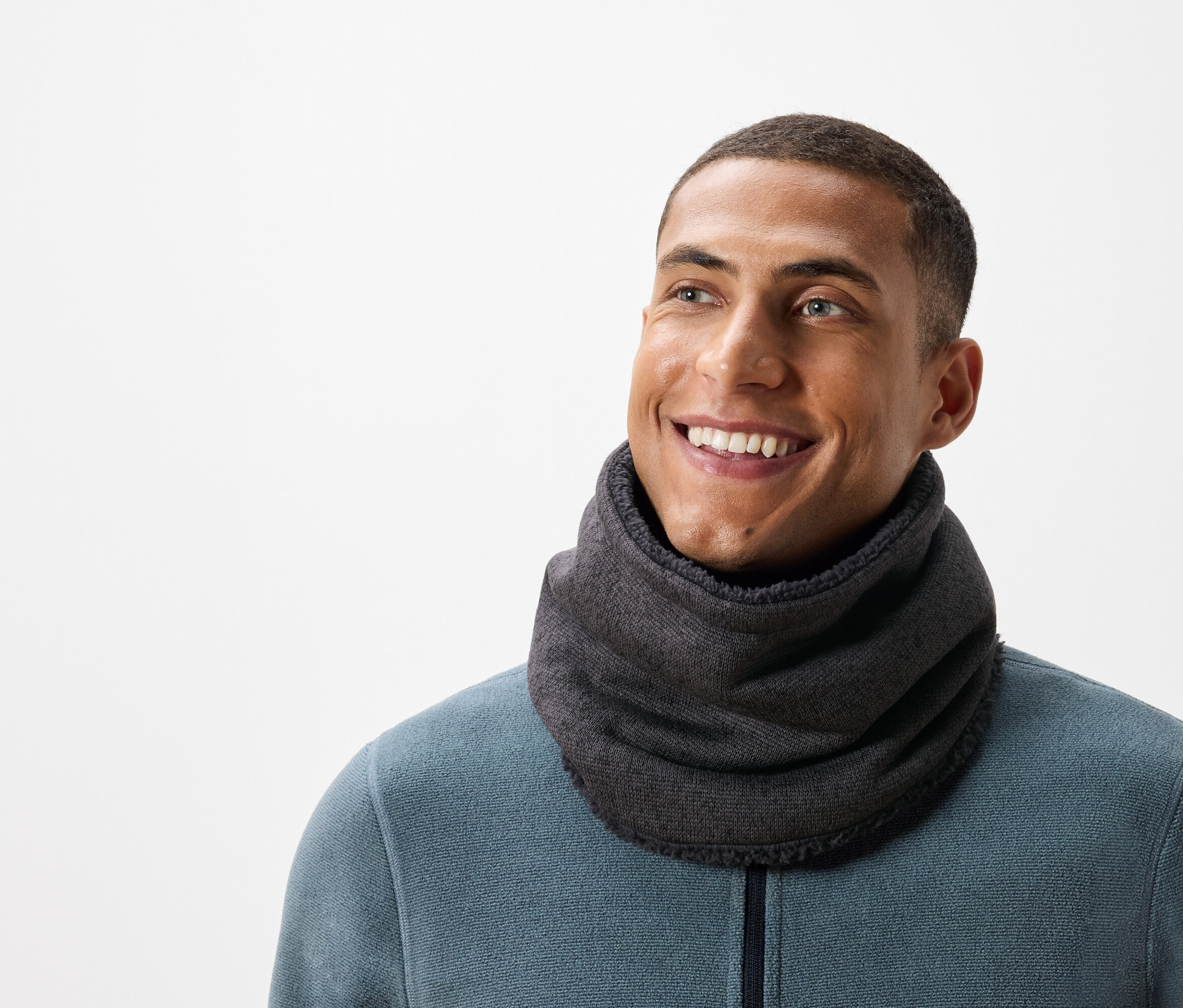 Lächelnder Mann mit kurzen Haaren trägt einen grauen Halswärmer und einen blaugrünen Pullover.