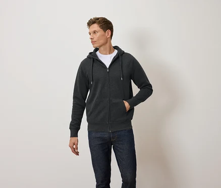 Mann trägt einen dunkelgrauen Kapuzenpullover mit Reißverschluss, ein weißes T-Shirt und blaue Jeans.