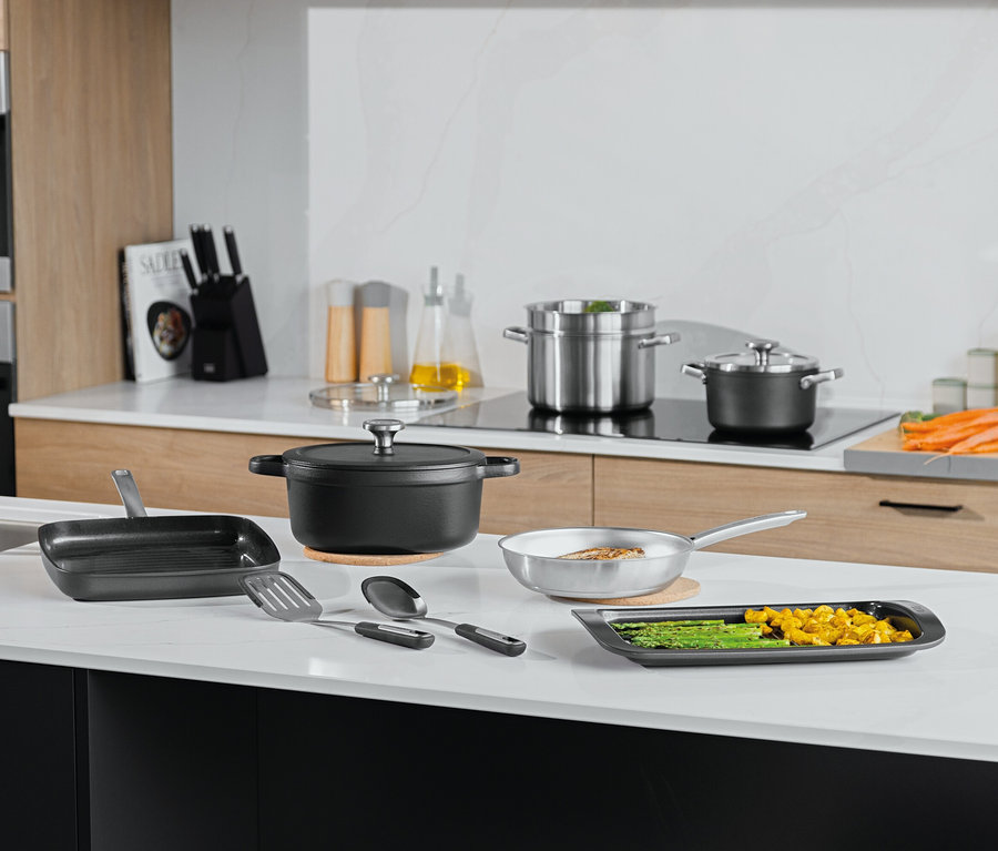 Verschiedene Kochtöpfe, Pfannen und Küchenutensilien auf einer weißen Küchentheke.