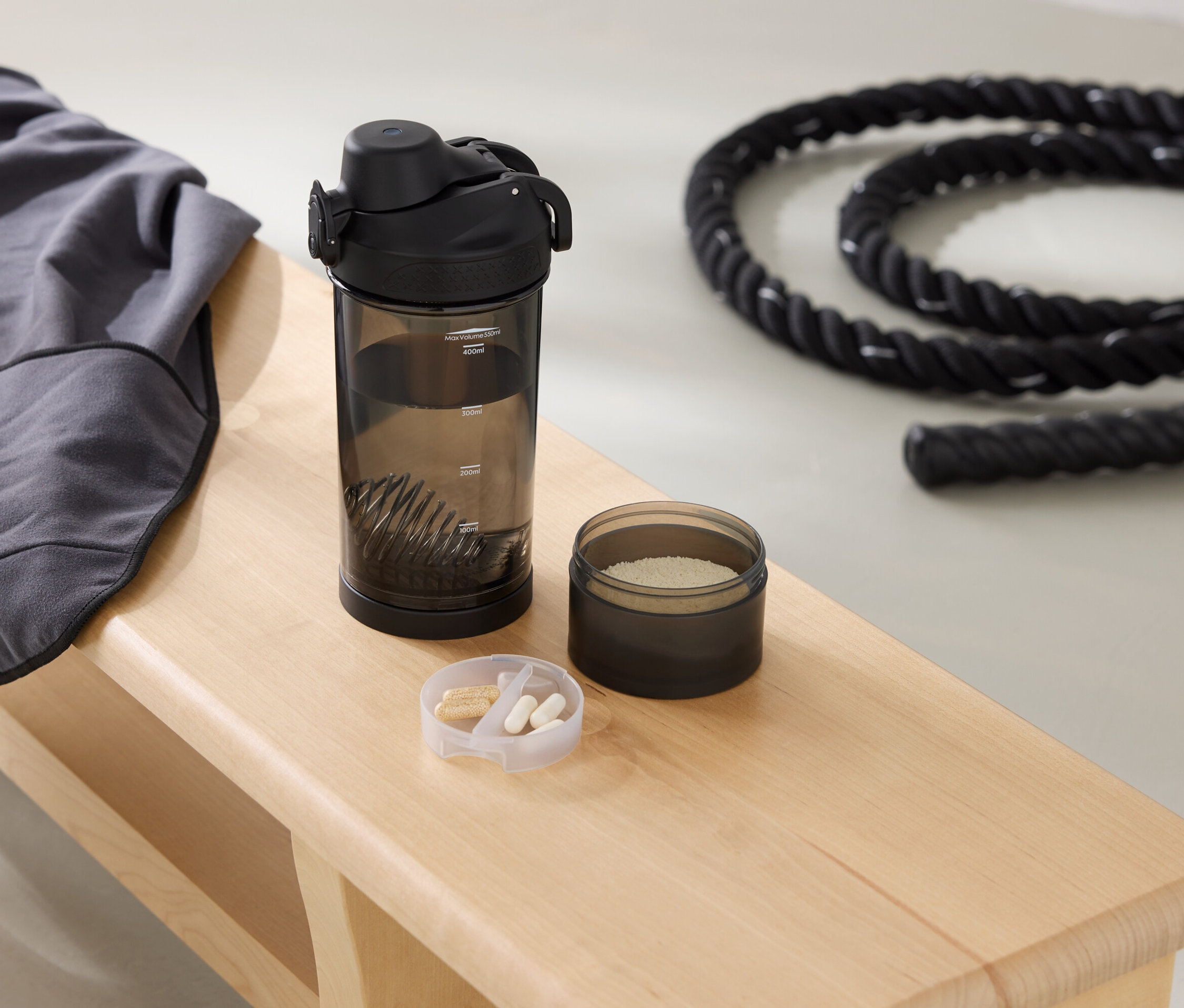 Auf einer Bank liegen ein graues Sweatshirt, eine Trinkflasche, eine Dose mit Pulver und ein Seil.