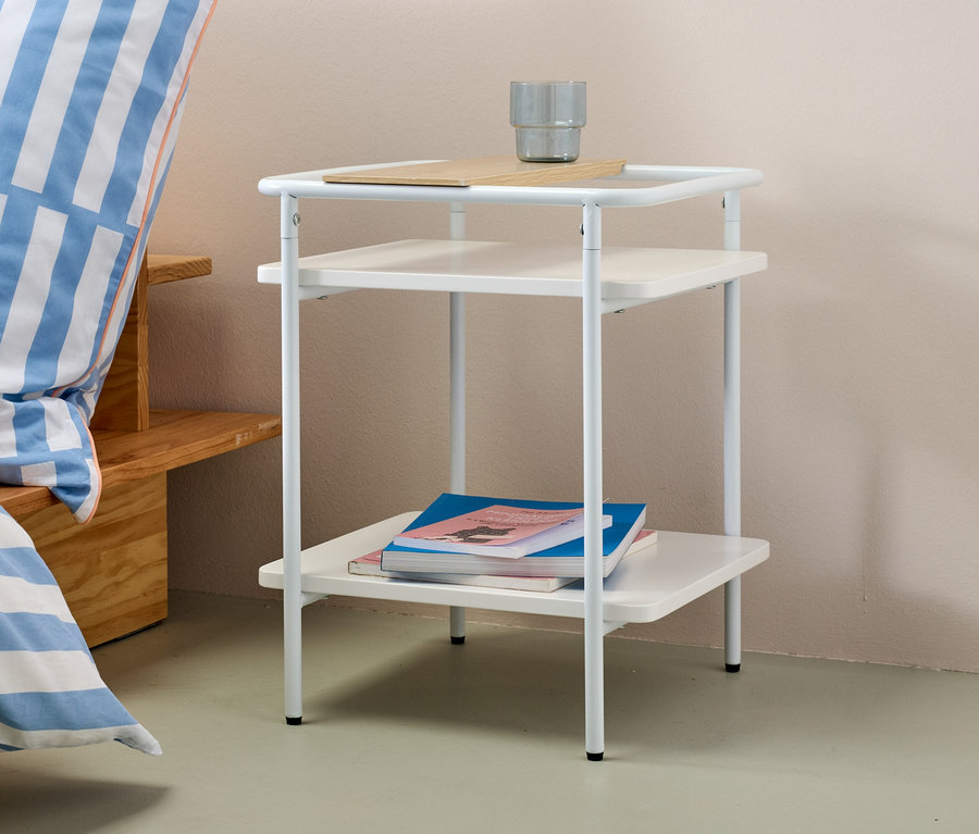 Weißer Beistelltisch mit zwei Ablagen und grauem Becher obenauf.