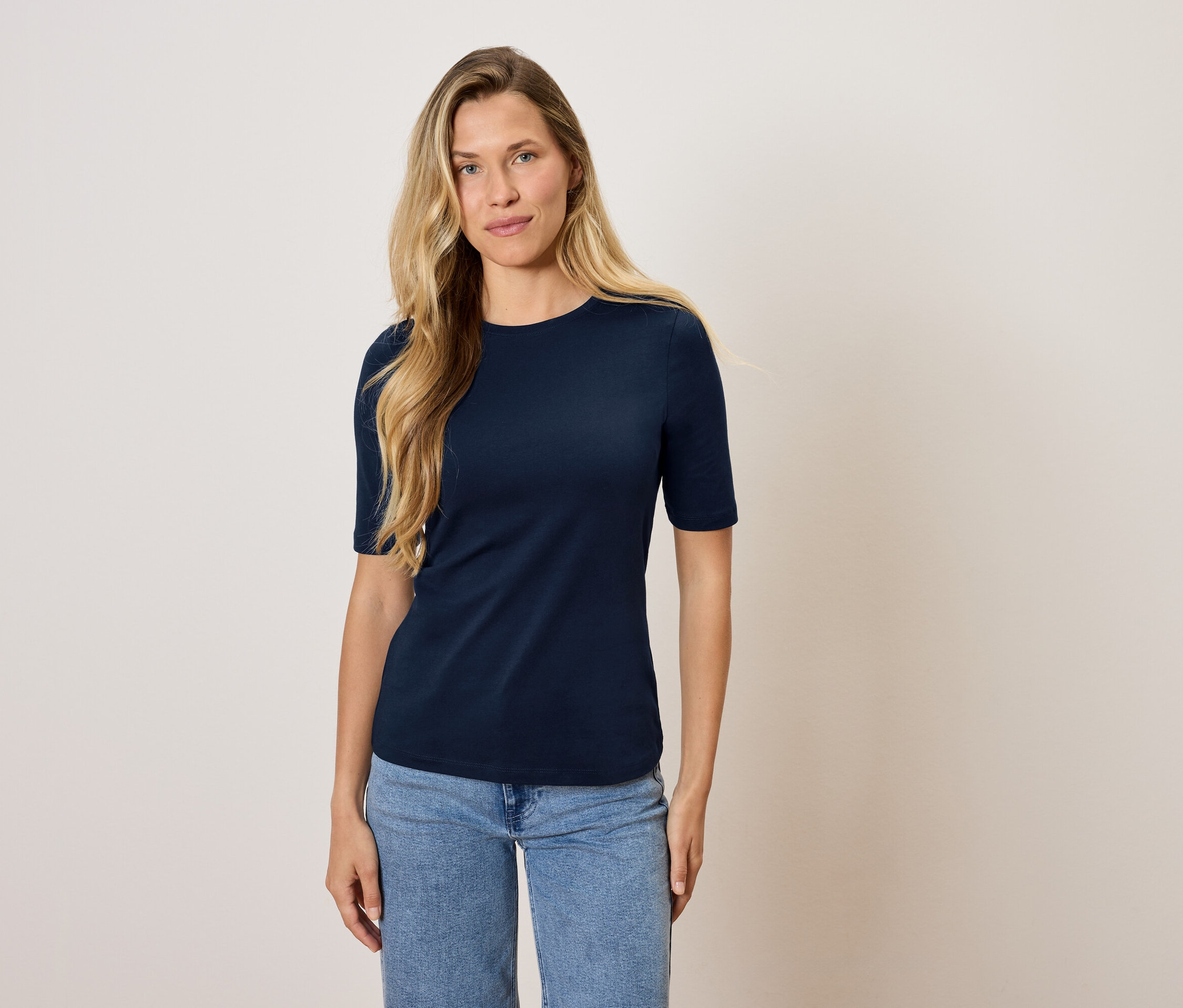 Eine Frau steht und trägt ein marineblaues T-Shirt und Jeans.