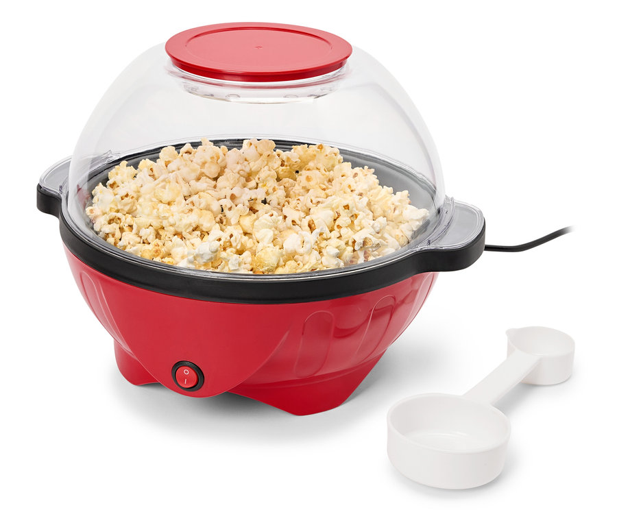 Ein roter Popcorn-Maker mit einem transparenten Deckel voller Popcorn und einem weißen Messbecher.