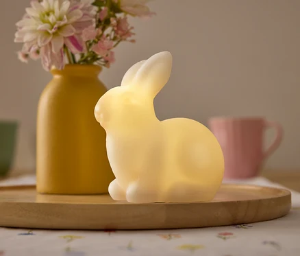 Gelbe Vase mit Blumen, gelbes Hasenlicht und Tassen auf einem Holztablett.