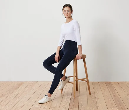 Eine Frau sitzt auf einem Holzhocker und trägt marineblaue Leggings und ein weißes Shirt.