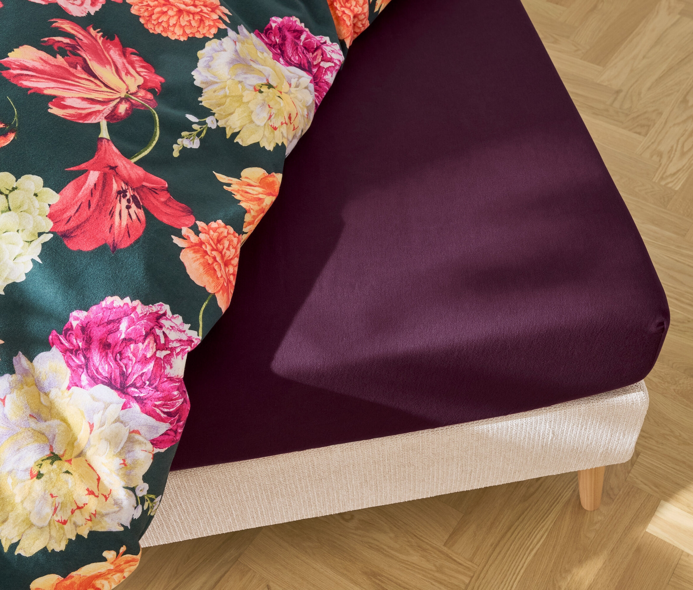 Bett mit lila Spannbettlaken und floraler Bettwäsche.