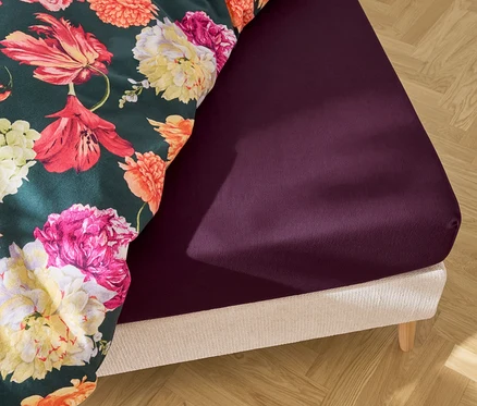 Bett mit lila Spannbettlaken und floraler Bettwäsche.