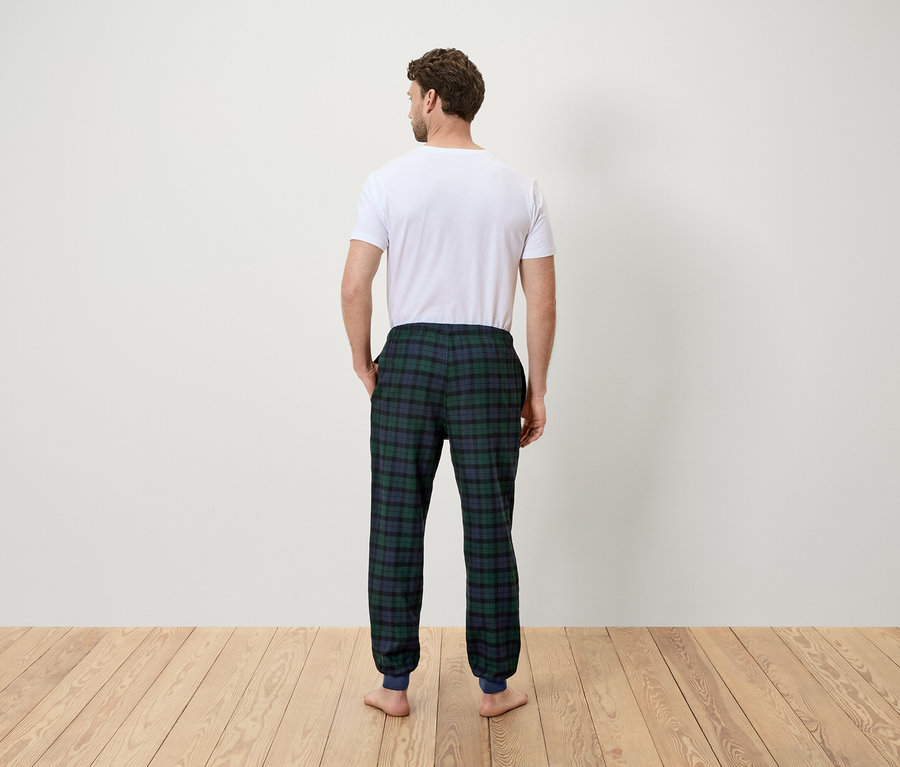 Mann von hinten trägt ein weißes T-Shirt und eine grün karierte Pyjamahose.