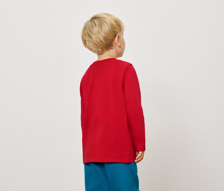 Blonder Junge von hinten in rotem Langarmshirt und blauer Hose.