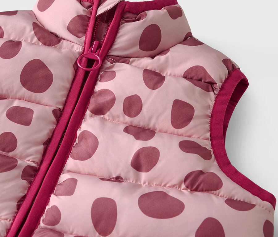 Detail einer rosa gesteppten Weste mit bordeauxfarbenen Punkten und Reißverschluss.