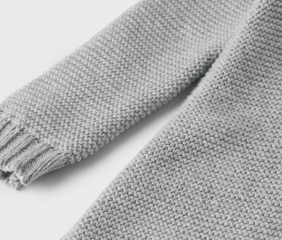 Detailansicht eines grauen Strickpullovers mit Ärmel und Bündchen.