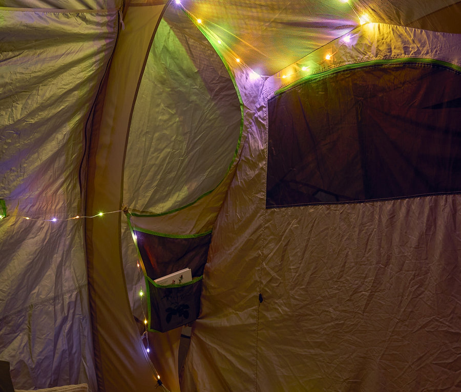 Innenansicht eines Zeltes, dekoriert mit bunten Lichtern, mit Kissen und einem Pouf im Vordergrund.