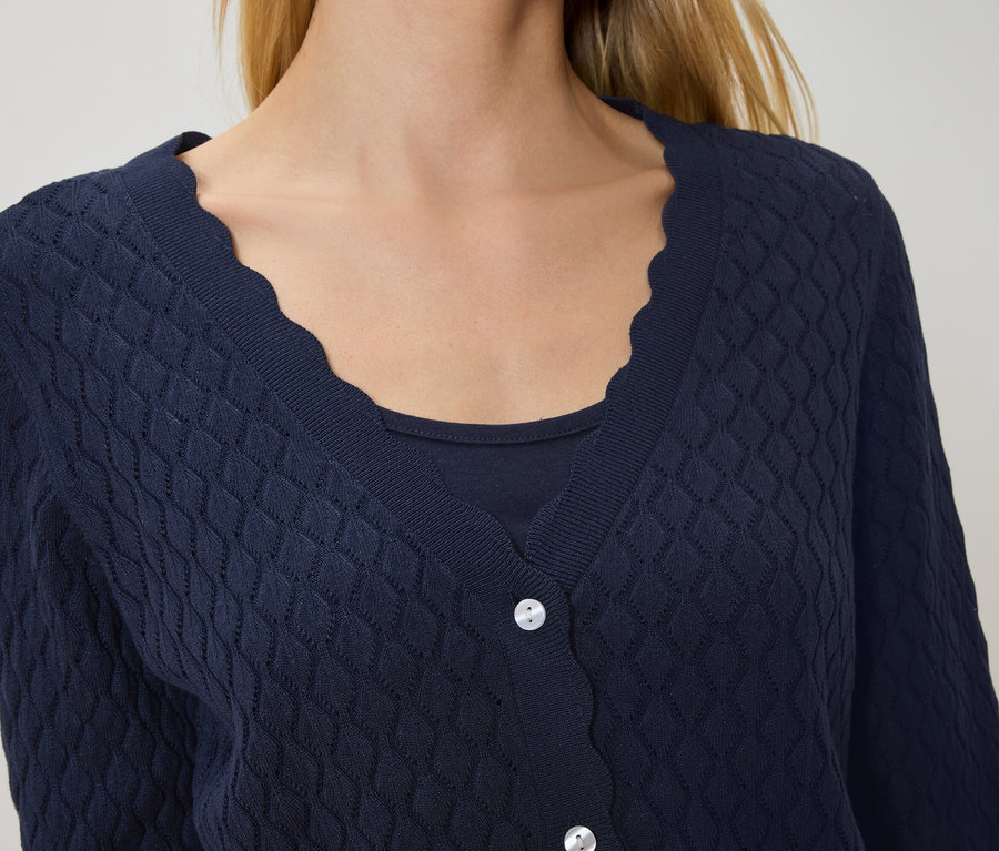 Frau trägt eine marineblaue Strickjacke mit gewelltem Saum über einem marineblauen Oberteil.