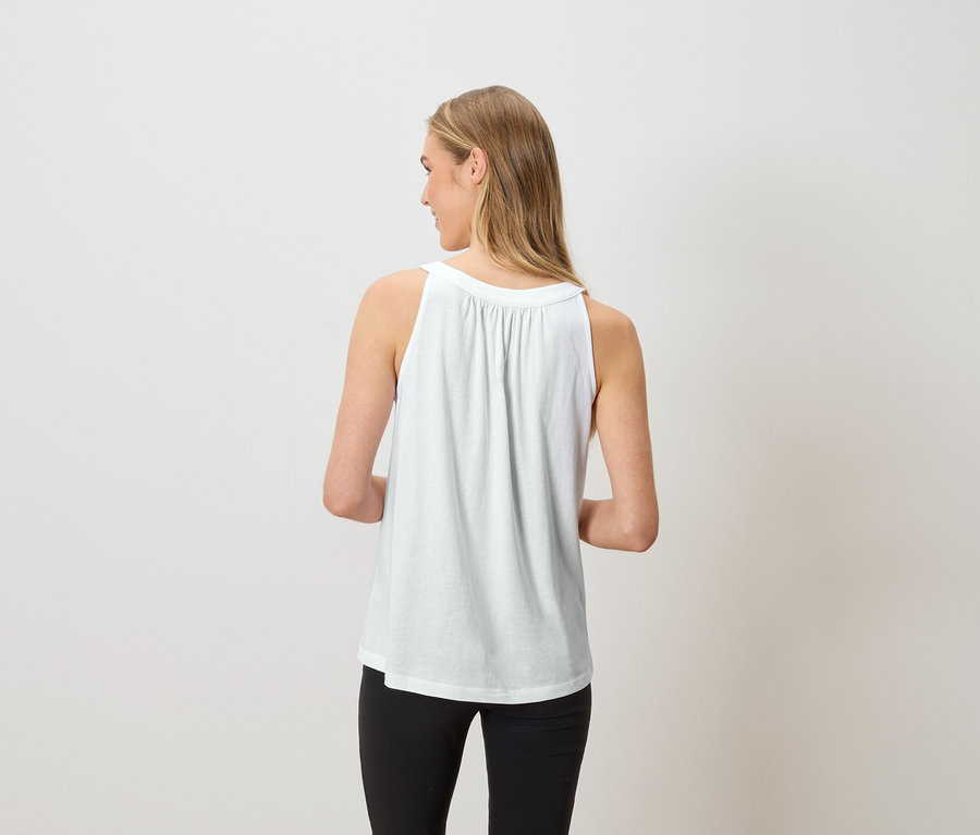 Frau von hinten, trägt ein weißes Tanktop und schwarze Hose.