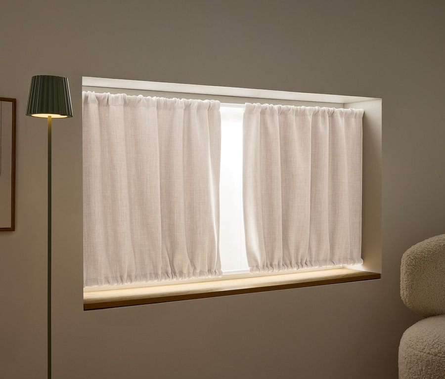 Blick auf ein Fenster mit beigen Vorhängen, eine grüne Stehlampe und ein abstraktes Kunstwerk an der Wand.