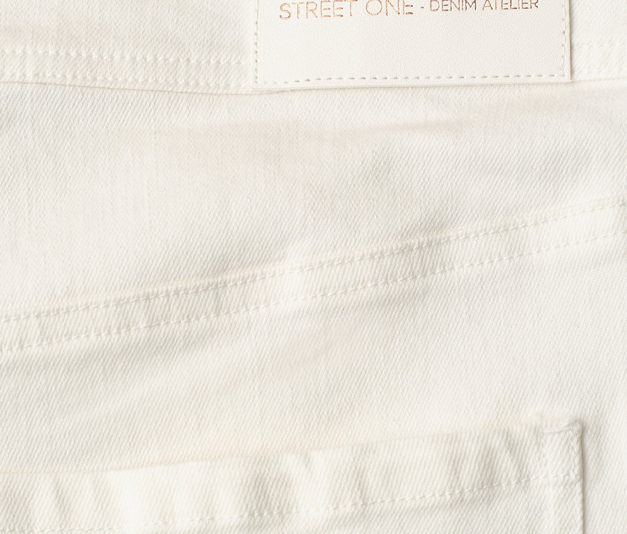 Nahaufnahme einer weißen Street One Jeans mit hellem Etikett, das 'designed with passion STREET ONE - DENIM ATELIER' zeigt.