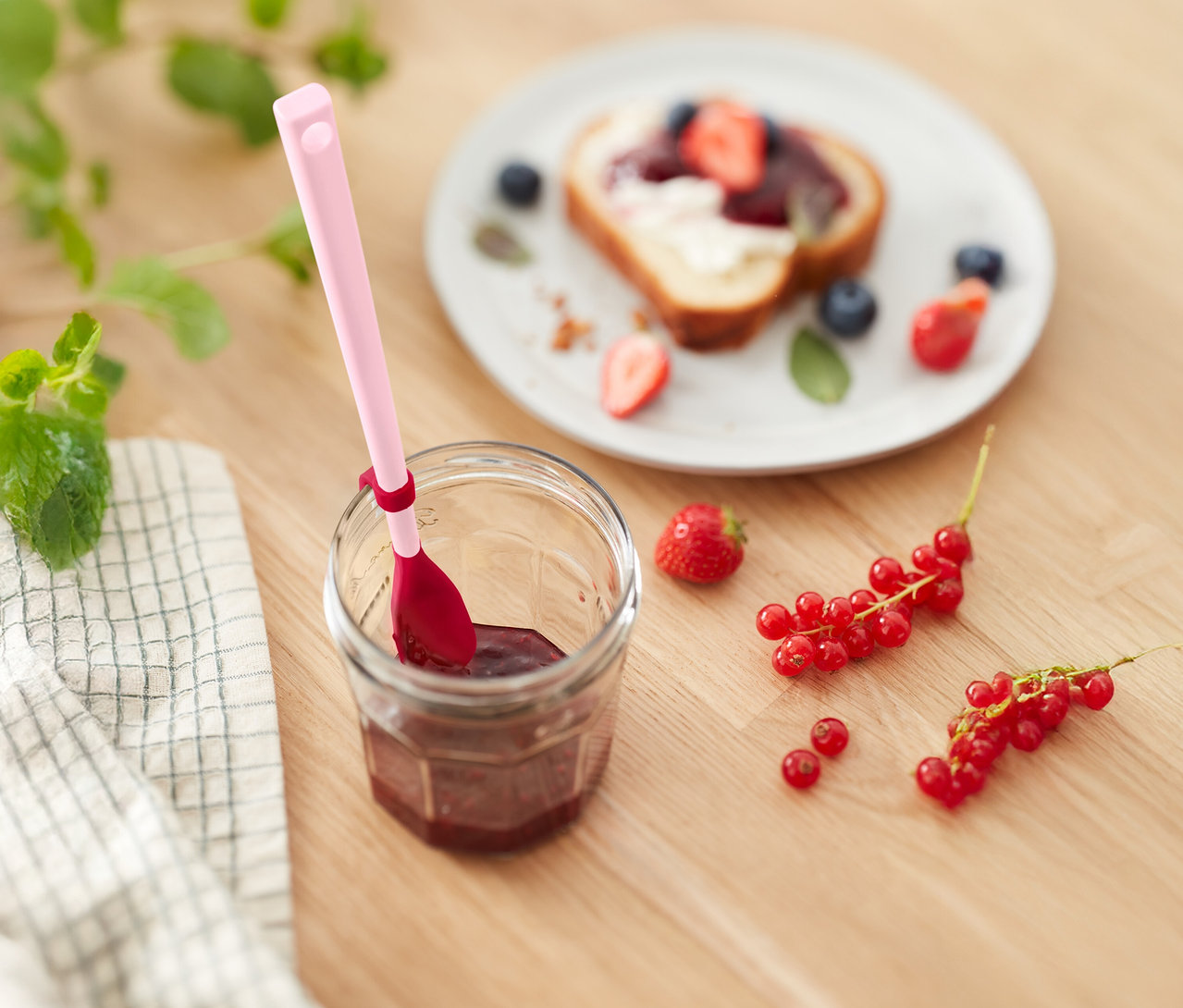 Marmeladenglas mit rosa Löffel, Toast mit Erdbeeren und Blaubeeren und Johannisbeeren auf einem Holztisch.